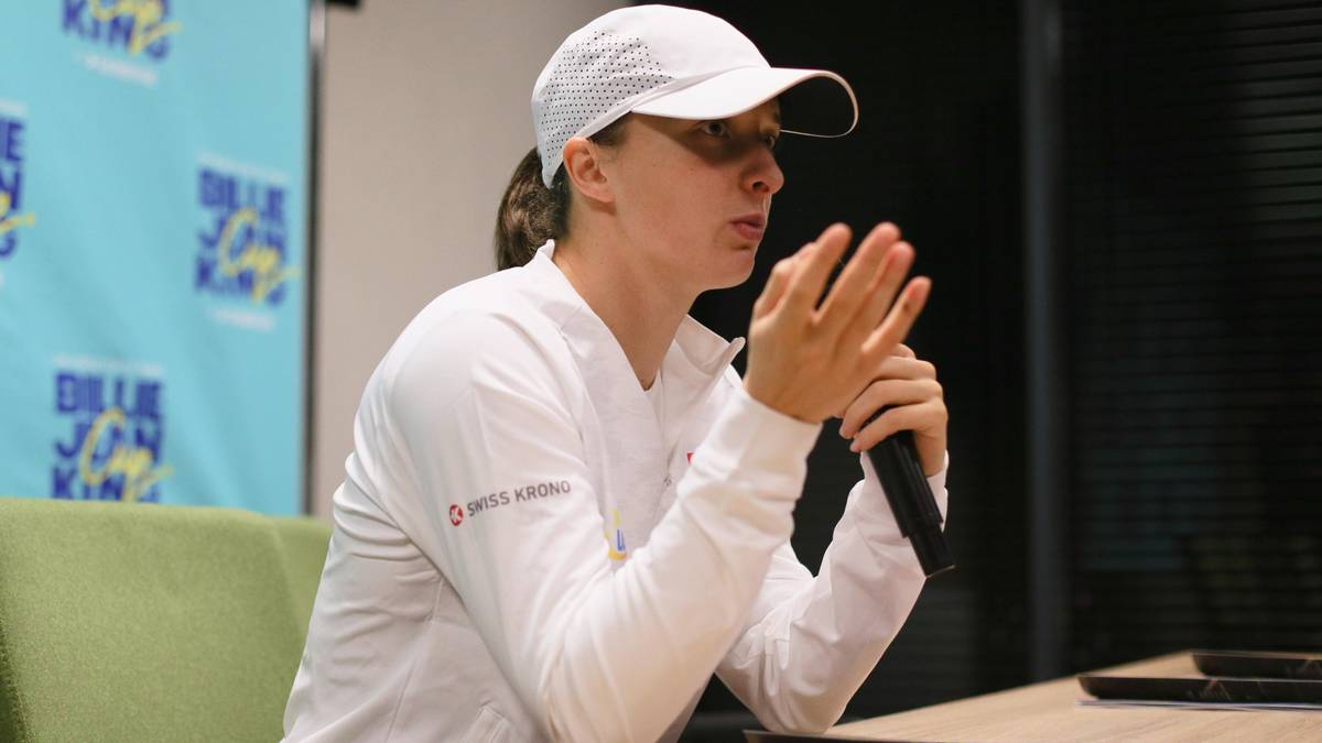 Kobieta w białej czapce i bluzie siedzi przy stole z mikrofonem.