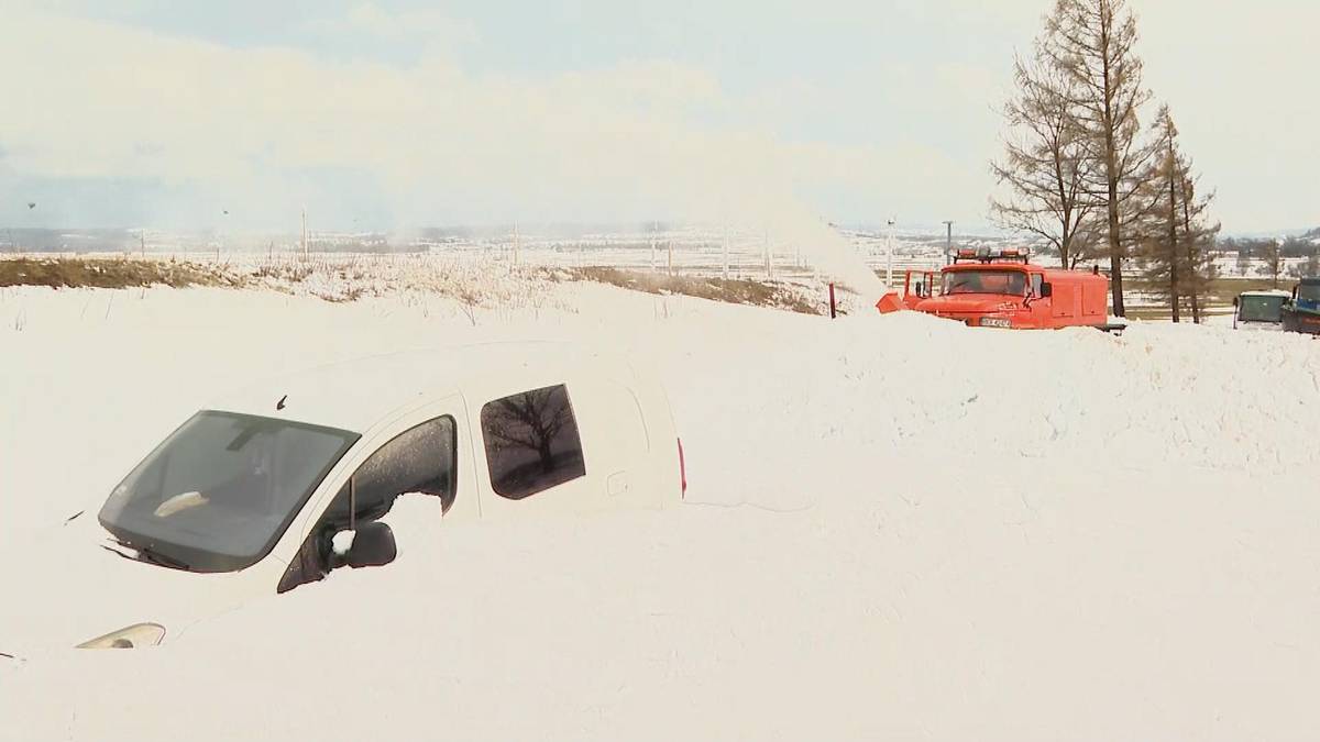 Samochód osobowy zasypany śniegiem, w tle pojazd strażacki z pługiem