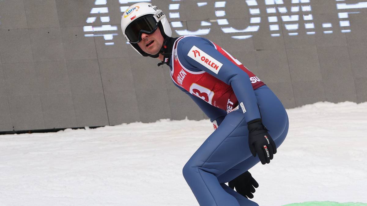 Skoczek narciarski w niebieskim kombinezonie i białym kasku przygotowuje się do skoku.