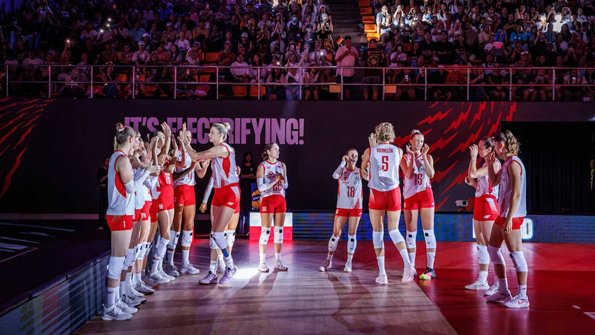 Drużyna siatkarek Polski w czerwonych strojach sportowych świętuje zwycięstwo na boisku przed pełnymi trybunami.