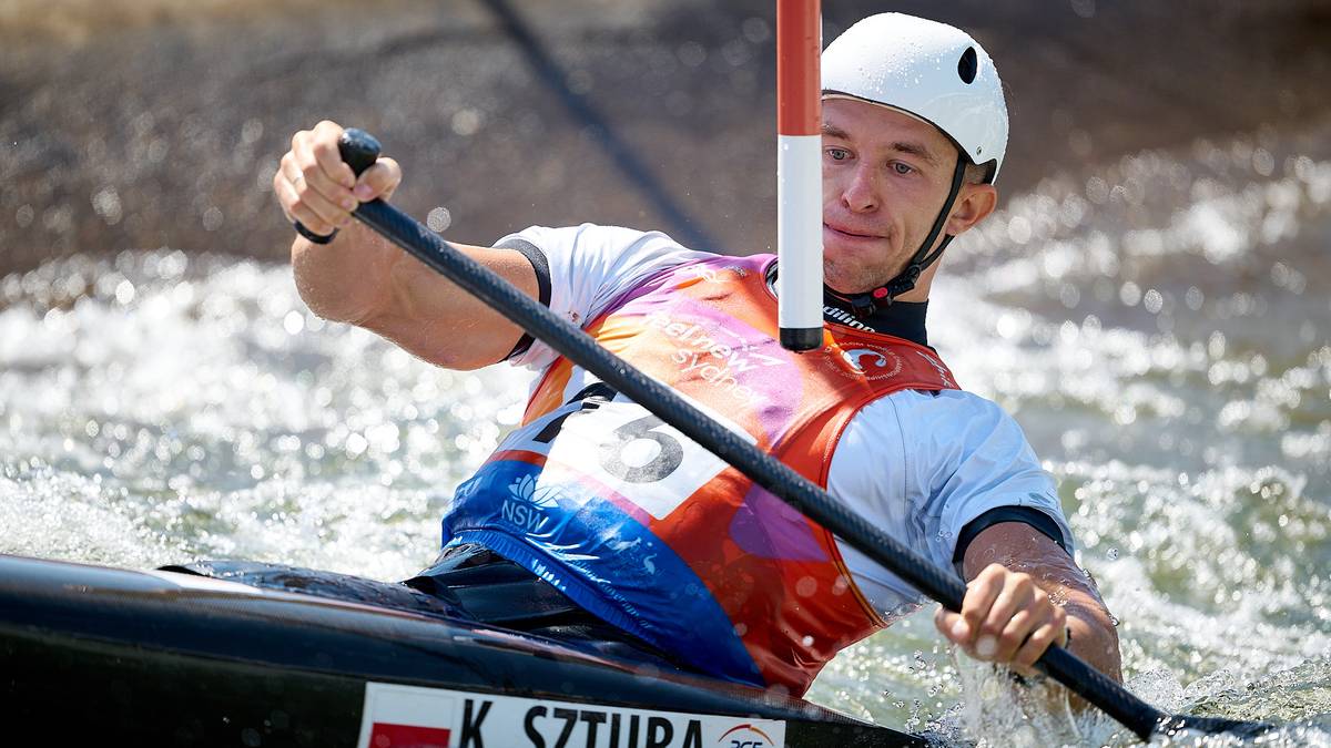 Mężczyzna w kasku i kamizelce pływackiej wiosłuje w kajaku po wzburzonej wodzie.