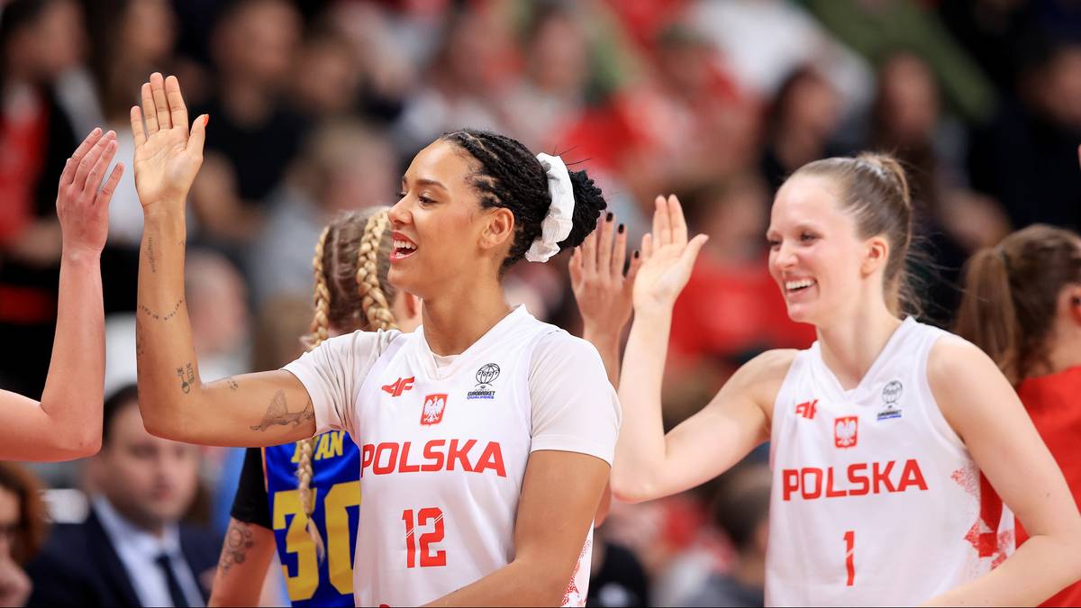 Dwie polskie koszykarki w białych strojach z numerami 12 i 1 podnoszą ręce, świętując na boisku.