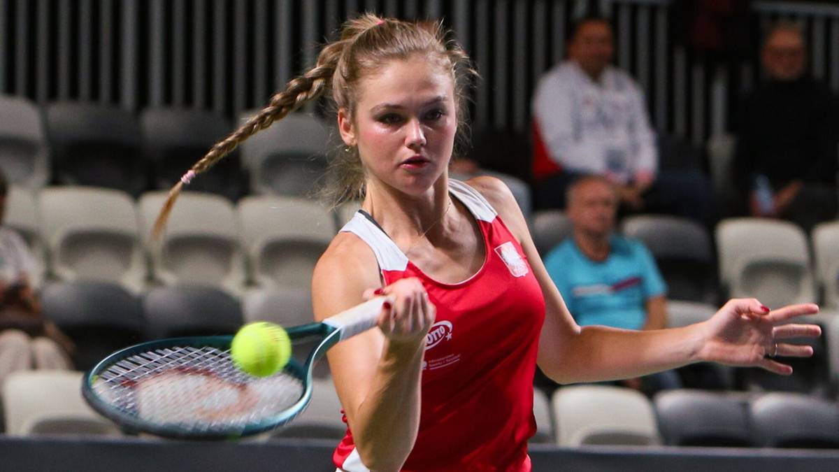 Tenisistka w stroju sportowym odbija piłkę rakietą podczas meczu.