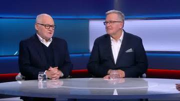 Dw&oacute;ch mężczyzn w garniturach siedzi przy stole, rozmawiając.