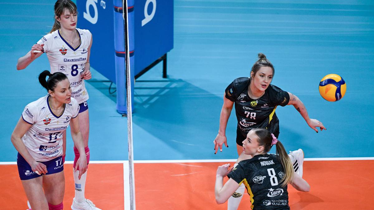 Siatkarki podczas meczu Tauron Ligi, jedna z nich przygotowuje się do zagrywki, a druga blokuje.