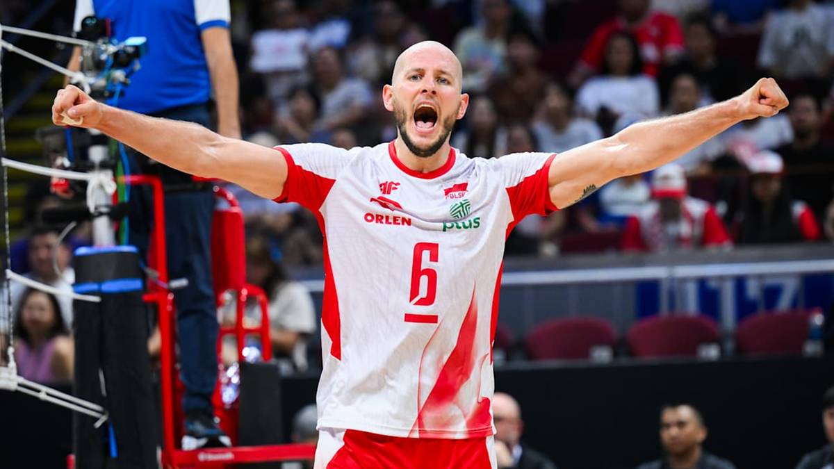 Siatkarz w biało-czerwonej koszulce z numerem 6 na piersi, z uniesionymi w górę pięściami i otwartymi ustami w geście radości lub krzyku, na tle trybun wypełnionych kibicami.