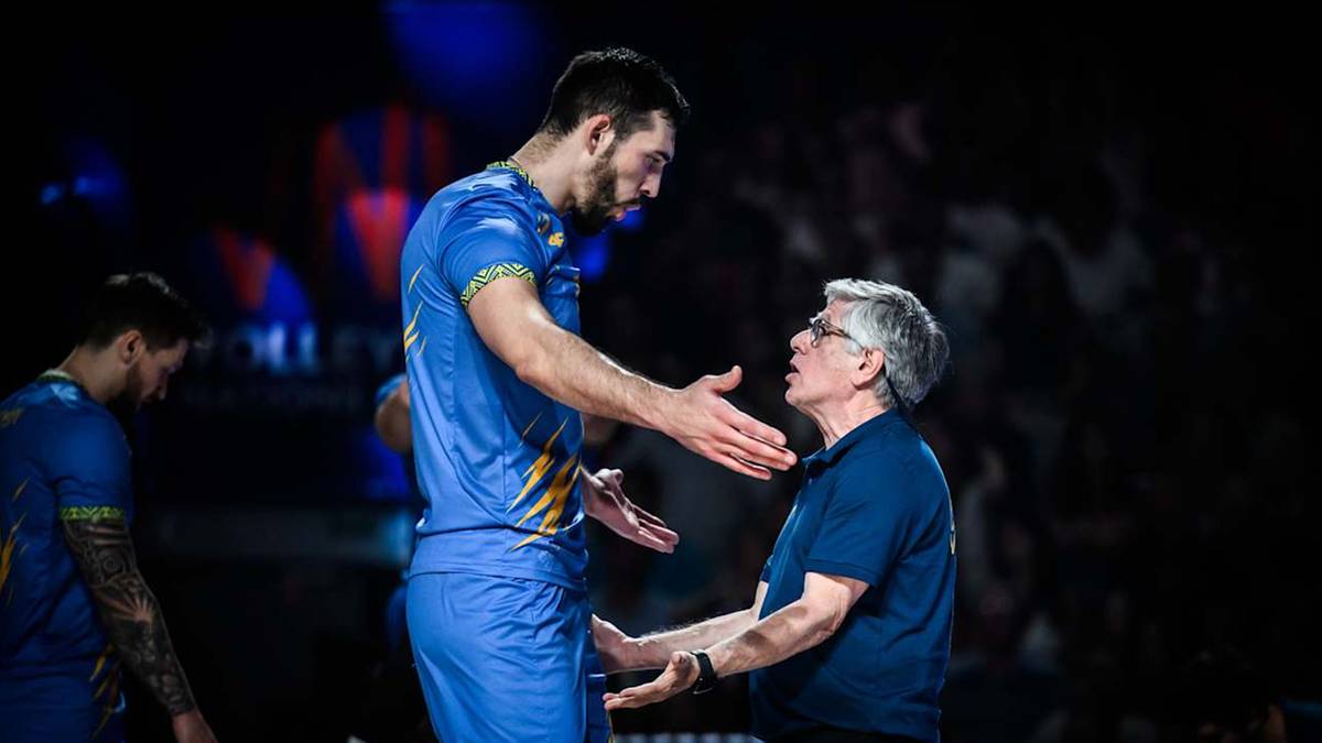 Trener rozmawia z wysokim siatkarzem w niebieskiej koszulce.