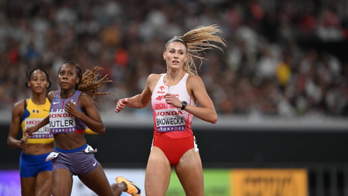 Zawodniczka w stroju biało-czerwonym biegnie do przodu, wyprzedzając inne lekkoatletki podczas zawodów.