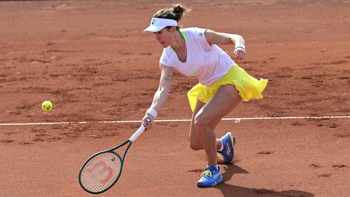 Tenisistka z rakietą w ręku, w ż&oacute;łtej sp&oacute;dniczce i białej koszulce, odbija piłkę na ceglanym korcie.