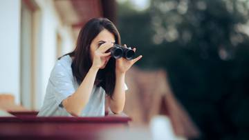 Kobieta wpatruje się przez lornetkę na zewnątrz.