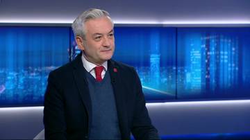 Mężczyzna w średnim wieku z siwymi włosami i w krawacie, siedzący przed ekranami z widokiem na nocne miasto.