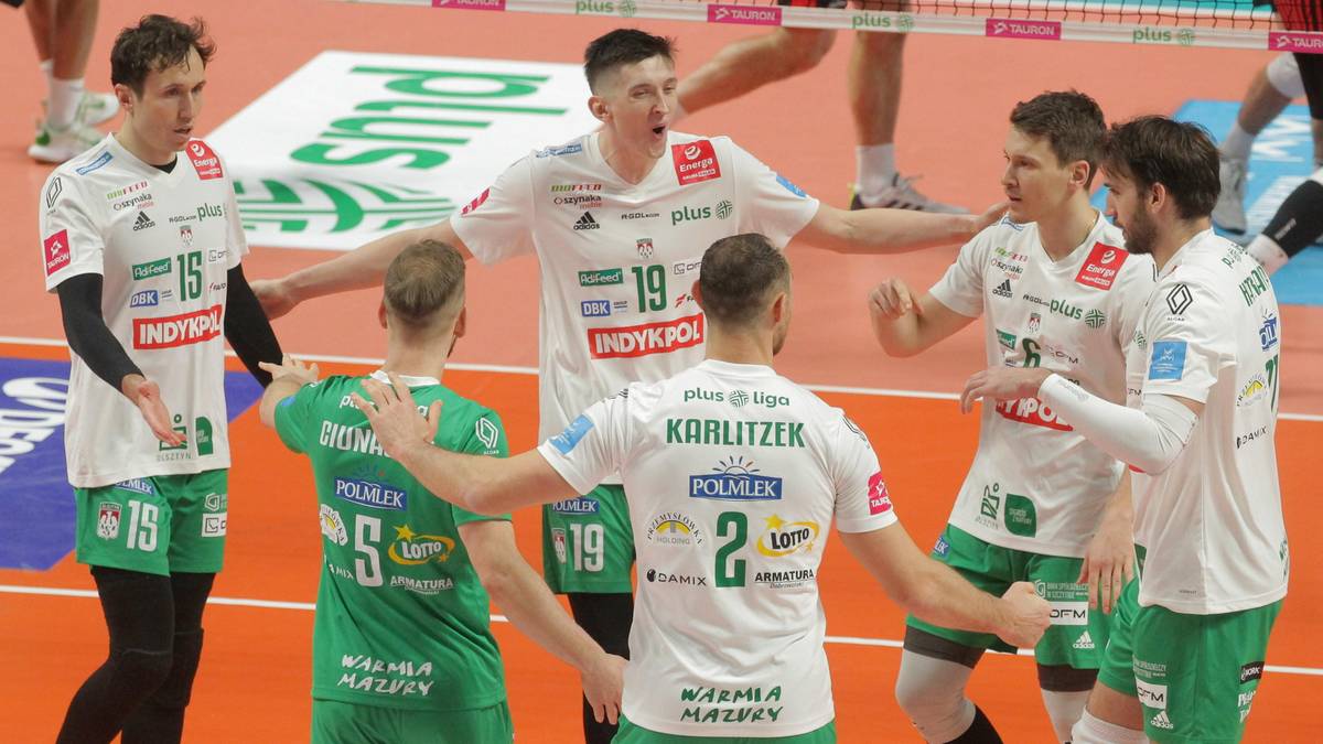 Siatkarze w białych strojach z zielonymi detalami celebrują zdobycie punktu na boisku siatkarskim.