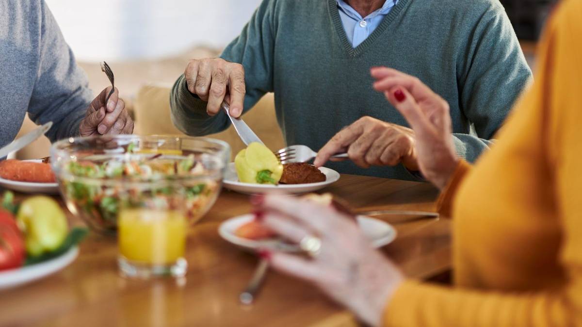 Osoby jedzące posiłek przy stole, skupiając się na talerzu z jedzeniem.