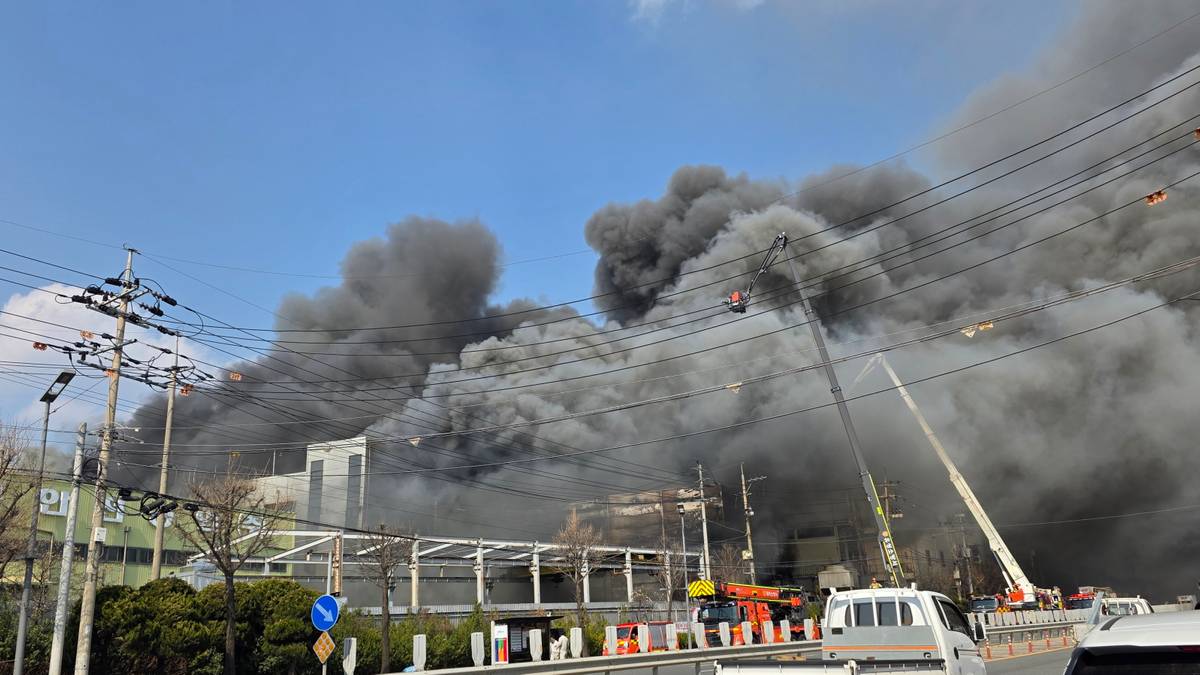 Gigantyczny słup dymu unoszący się nad fabryką części samochodowych w Korei Południowej, widoczne wozy strażackie i podnośniki.
