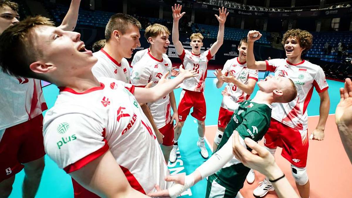 Drużyna siatkarzy w białych koszulkach świętuje zwycięstwo, jeden z zawodników jest podnoszony na rękach.