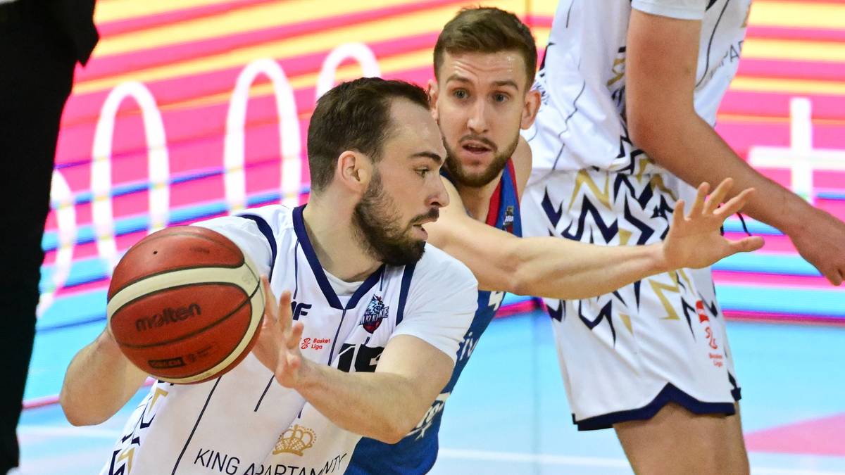 Koszykarz z piłką i dwoma rywalami na boisku podczas meczu.