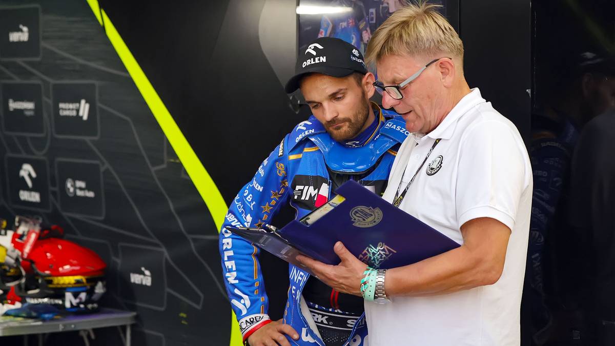 Dwóch mężczyzn w strojach żużlowych i sportowym ubraniu ogląda dokument.