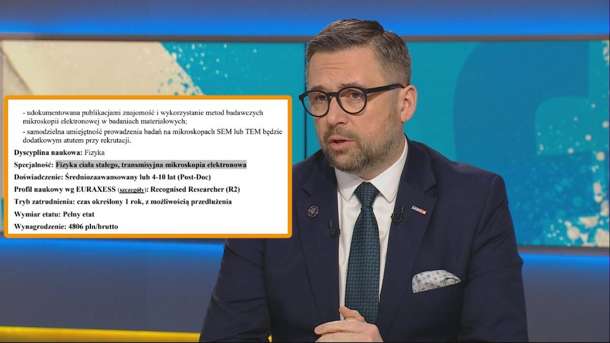 Mężczyzna w okularach i garniturze stoi przed ekranem z tekstem oferty pracy z Instytutu Fizyki PAN.