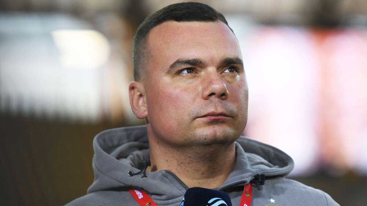 Portret mężczyzny w szarej bluzie z kapturem, ubranego w strój sportowy.