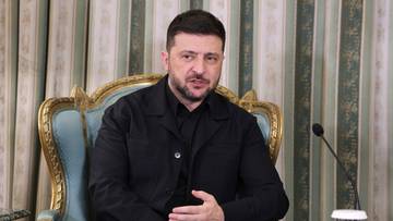 Wołodymyr Zełenski siedzi na ozdobnym krześle w czarnej koszuli i zamyślonym wyrazem twarzy.