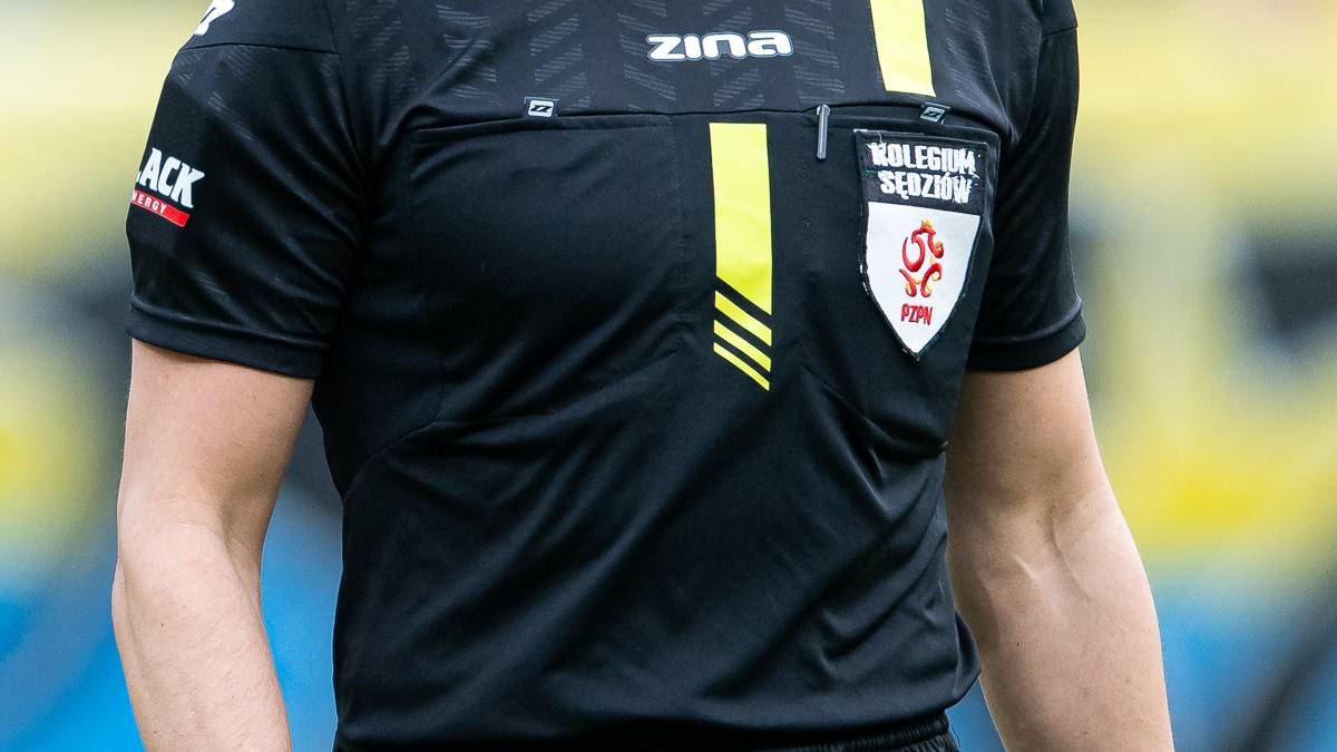Sędzia piłkarski w czarnej koszulce i spodenkach na boisku.