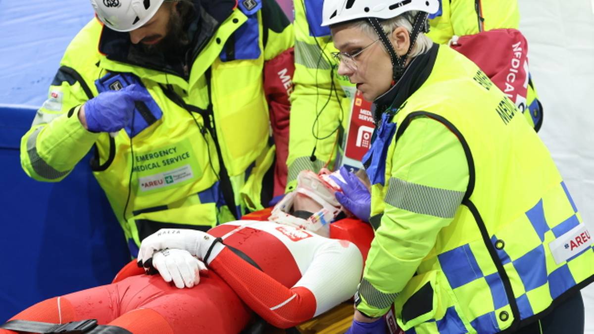 Zawodniczka na noszach z opatrunkiem na twarzy, otoczona przez ratownik&oacute;w medycznych w ż&oacute;łtych kamizelkach.