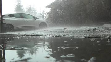 Samoch&oacute;d zaparkowany na zewnątrz podczas intensywnego deszczu i gradu.