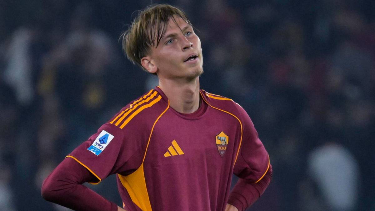 Młody piłkarz w burgundowej koszulce AS Romy z ż&oacute;łtymi pasami na rękawach i kołnierzyku, z numerem 77, spogląda w g&oacute;rę z wyrazem zmartwienia na twarzy. Na piersi widoczne logo Serie A i herb klubu.