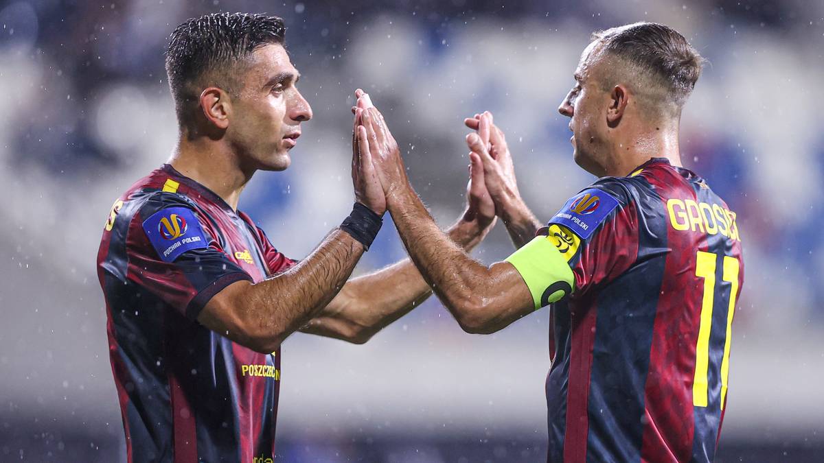 Dw&oacute;ch piłkarzy w kolorowych strojach sportowych grających w piłkę nożną, klaszczących w dłonie na znak gratulacji.