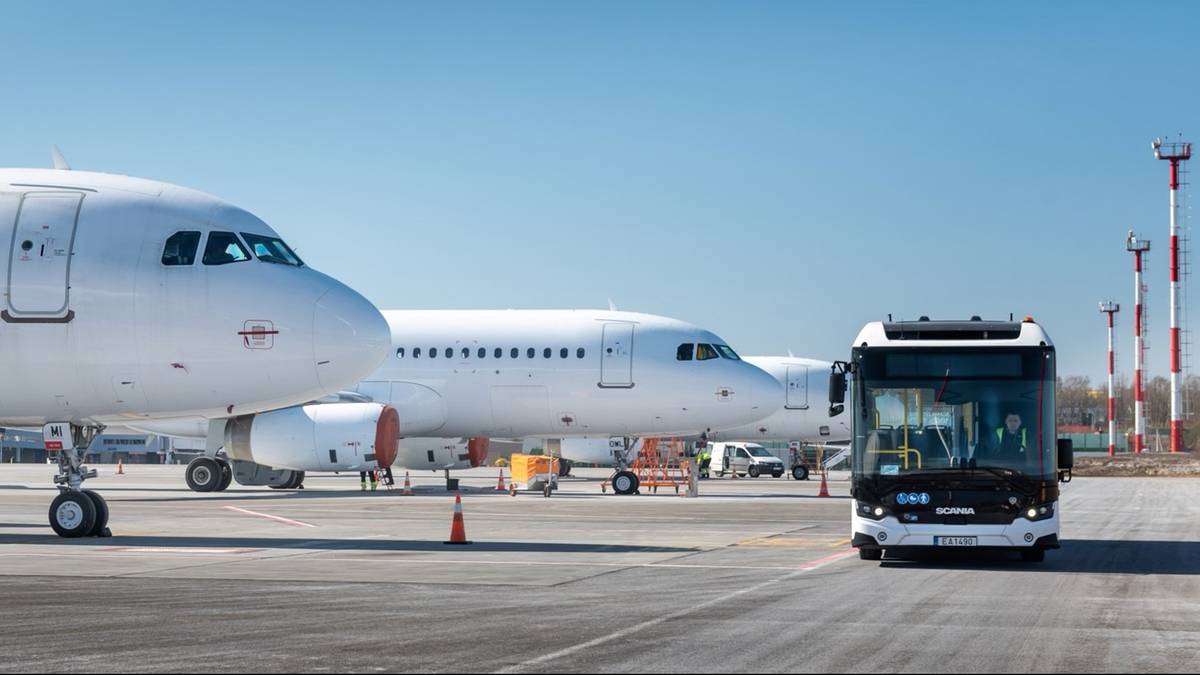 Dwa białe samoloty pasażerskie na płycie lotniska, z autobusem w tle.