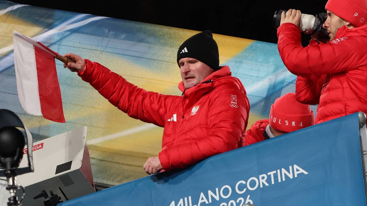 Trener Maciej Maciusiak trzyma polską flagę, ubrany w czerwoną kurtkę z biało-czerwonym godłem.