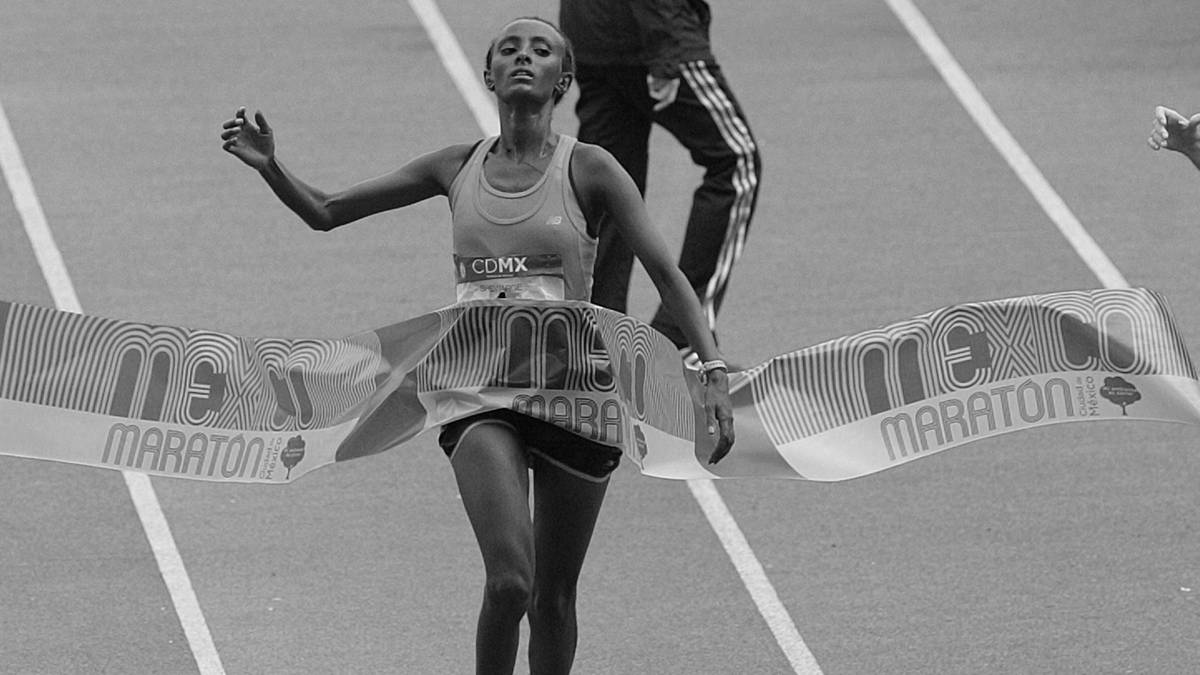 Kobieta biegnie i przekracza linię mety maratonu.