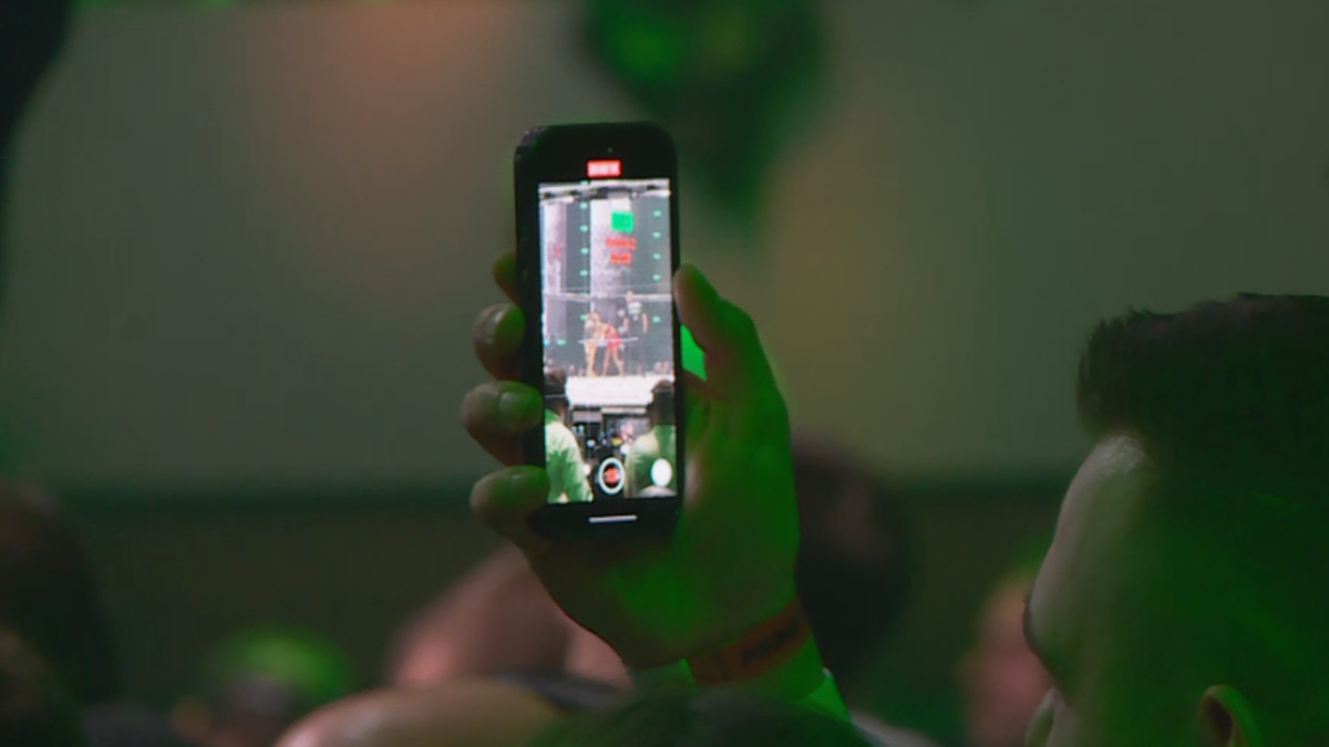 Dłoń trzymająca smartfon nagrywający wydarzenie na scenie.