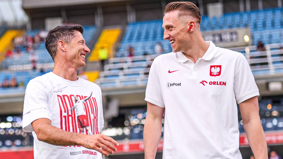 Dwóch mężczyzn w koszulkach piłkarskich uśmiecha się do siebie. Jeden ma białą koszulkę z napisem, drugi białą koszulkę z godłem Polski.