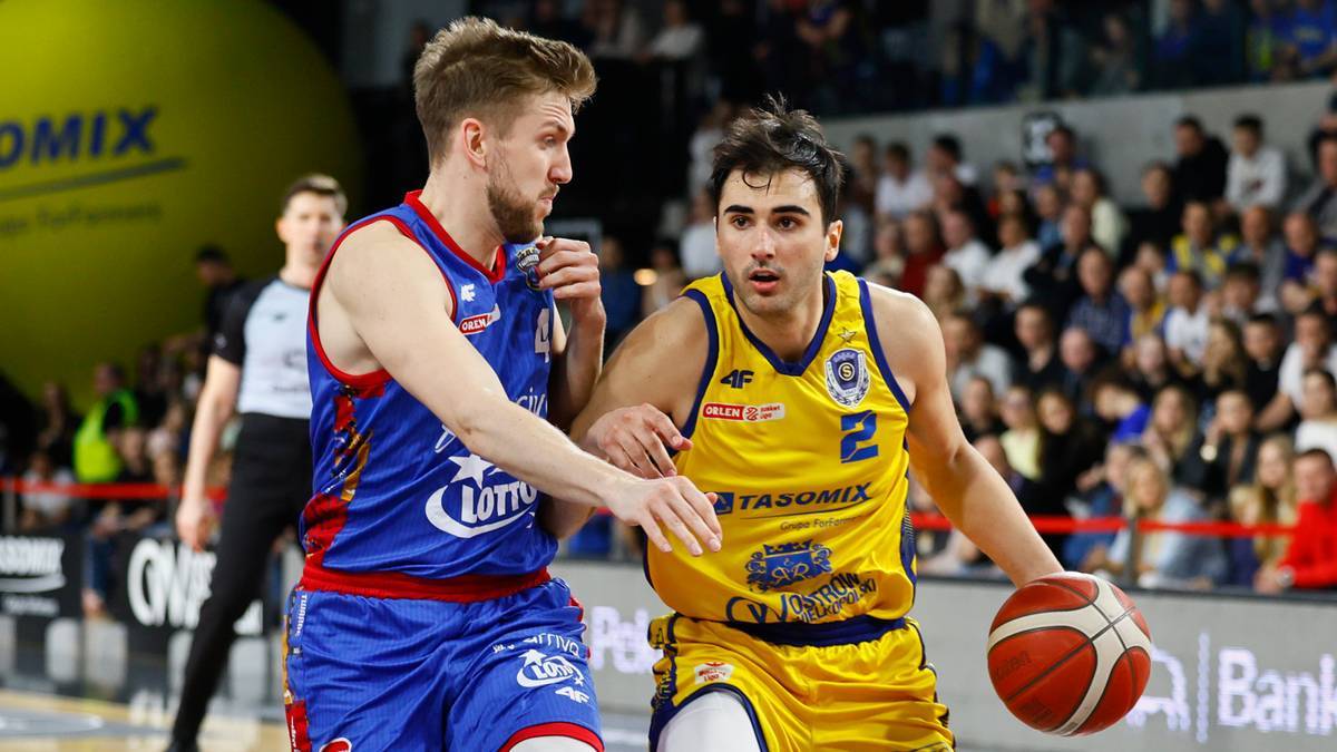 Dw&oacute;ch koszykarzy walczących o piłkę podczas meczu, jeden w ż&oacute;łtym stroju z numerem 2 na plecach, drugi w niebiesko-czerwonym stroju.
