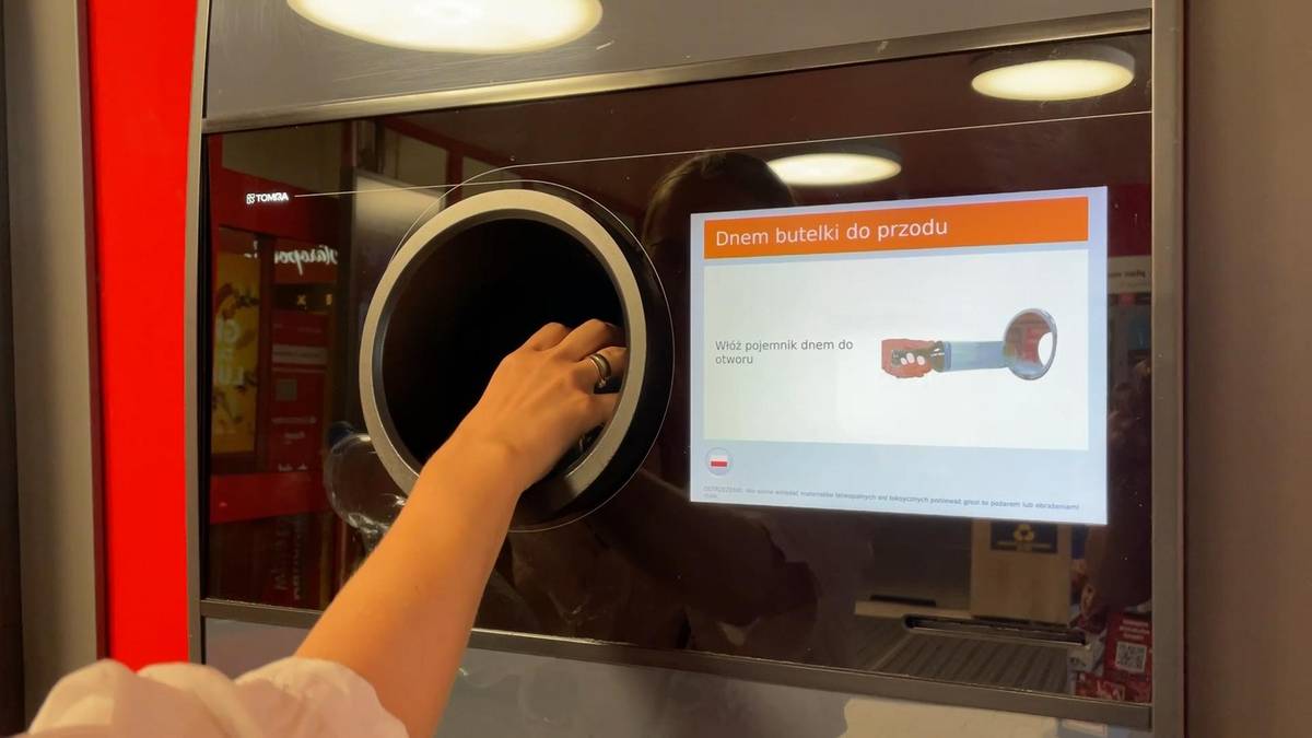 Dłoń wkładająca plastikową butelkę do otworu maszyny do zwrotu opakowań.