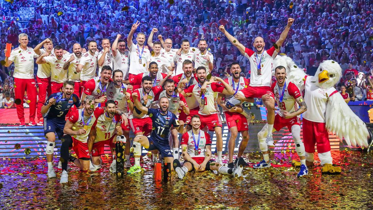 Drużyna piłkarzy ręcznych w czerwono-białych strojach świętuje na boisku, trzymając puchary i medale, podczas gdy tłum kibiców obserwuje z trybun.