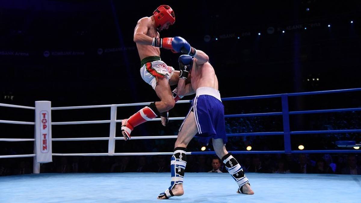 Dwóch zawodników kickboxingu walczy na ringu, jeden wykonuje wysokie kopnięcie.