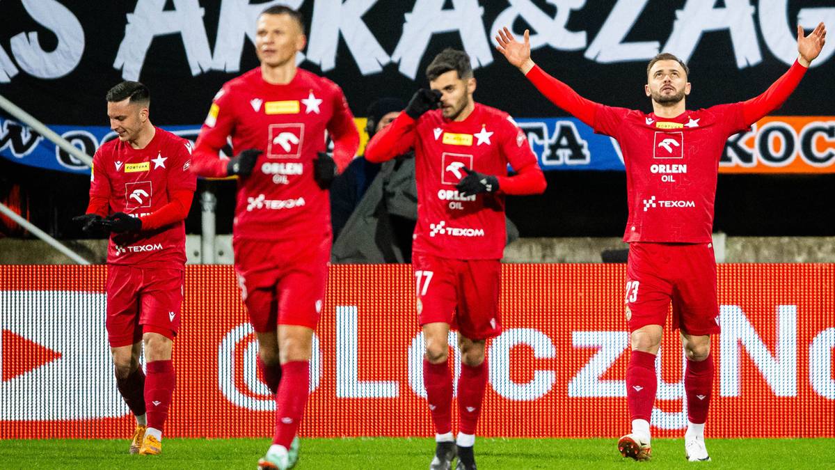 Czterech piłkarzy w czerwonych strojach z herbem Wisły Kraków biegnie w stronę trybun, wykonując gesty radości.