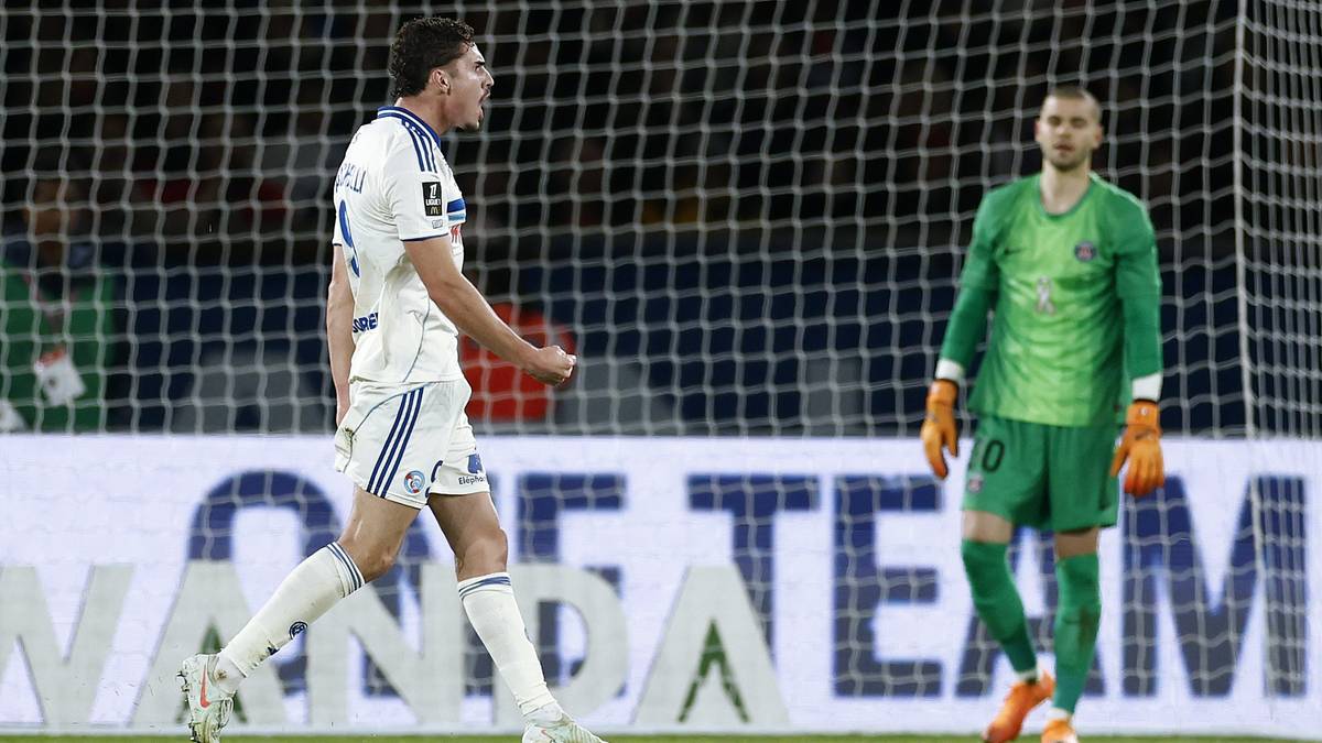 Piłkarz w białej koszulce z numerem 24 i niebieskimi pasami, biegnie w kierunku bramki. Po prawej stronie stoi bramkarz w zielonym stroju.