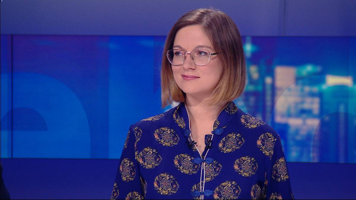 Kobieta w okularach i bluzce w wzory siedzi przed niebieskim tłem