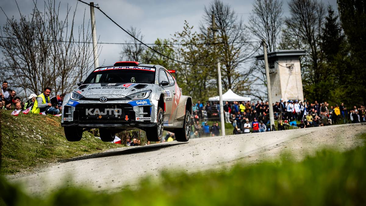 Samoch&oacute;d rajdowy w powietrzu podczas rajdu, z widownią po bokach drogi.