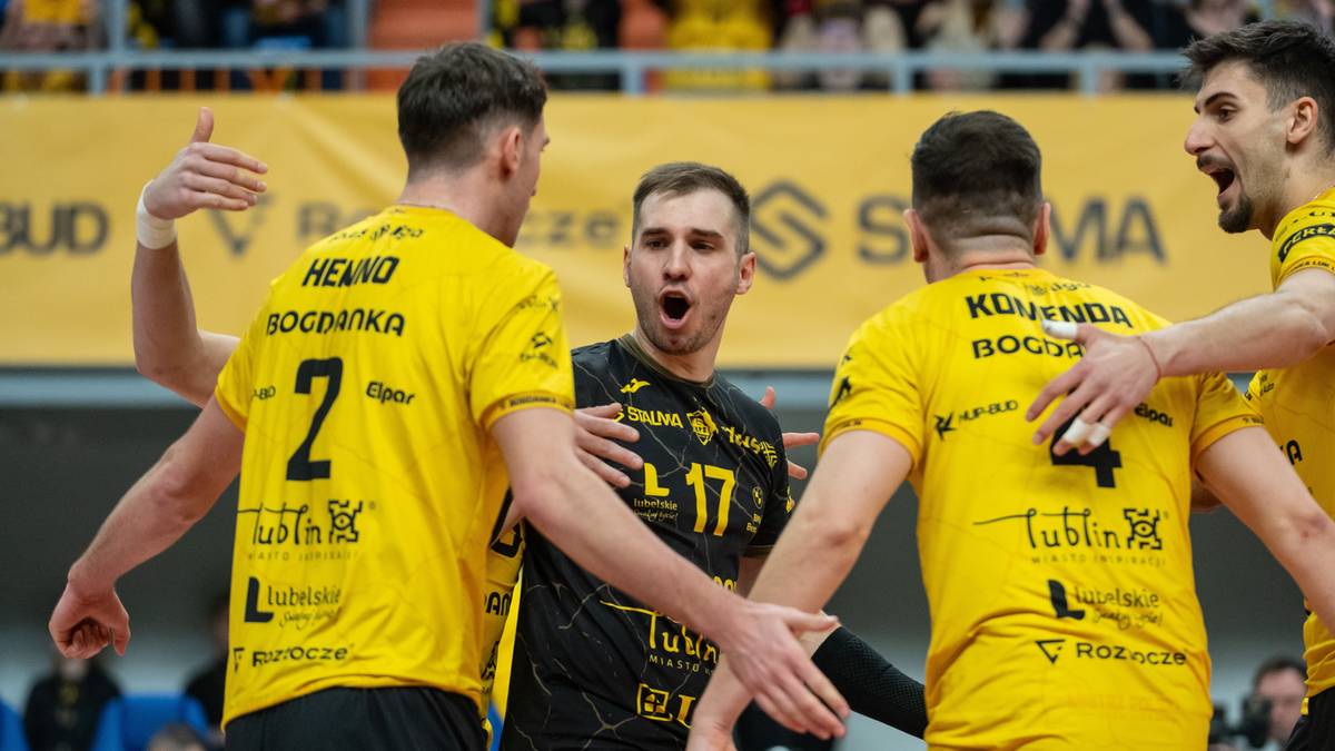 Siatkarze drużyny Bogdanka LUK Lublin w żółtych strojach sportowych świętują razem z zawodnikiem w czarnym stroju.