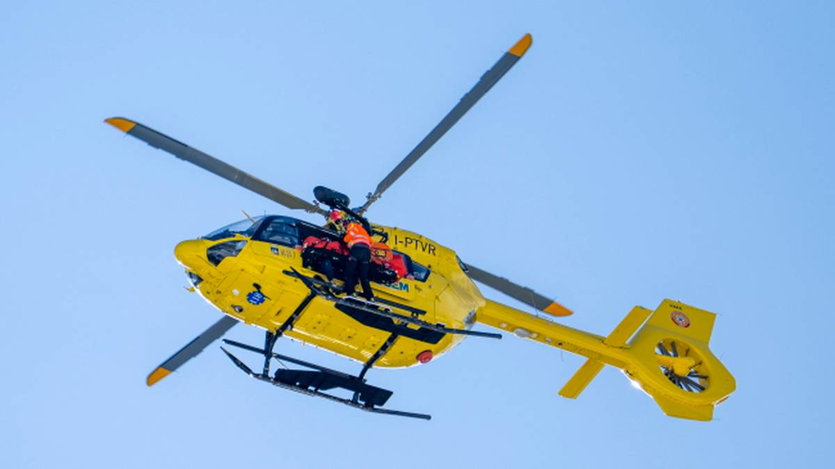 Ż&oacute;łty helikopter ratunkowy z załogą w środku latający na tle błękitnego nieba.