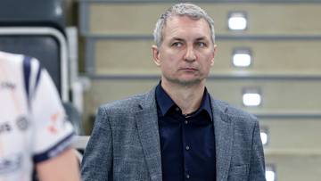 Mężczyzna w garniturze stojący na tle trybun hali sportowej.