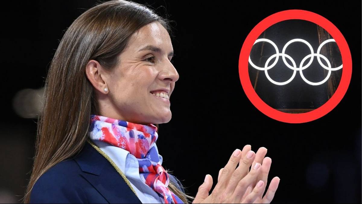 Uśmiechnięta kobieta w garniturze i kolorowym szaliku, obok niej widnieje czerwone koło z białymi symbolami kół olimpijskich.