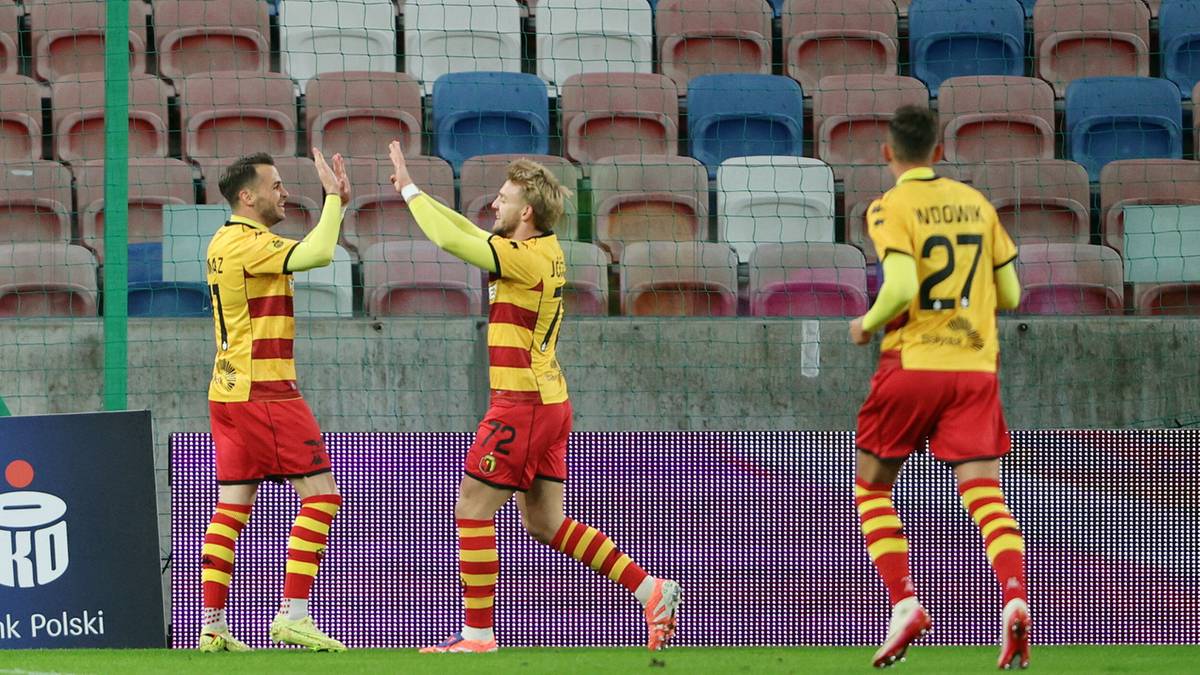 Trzech piłkarzy w ż&oacute;łtych koszulkach z czerwonymi pasami i czerwonych spodenkach świętuje gola. Dw&oacute;ch zawodnik&oacute;w podaje sobie dłonie w geście radości, a trzeci biegnie w ich stronę z uniesionymi rękami.