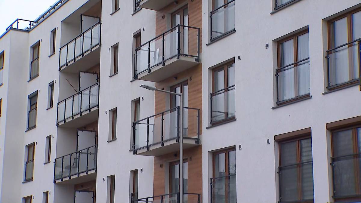 Fragment fasady nowoczesnego bloku mieszkalnego z licznymi balkonami i oknami.