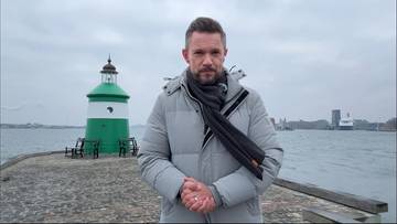 Mężczyzna stojący na molo przed latarnią morską.