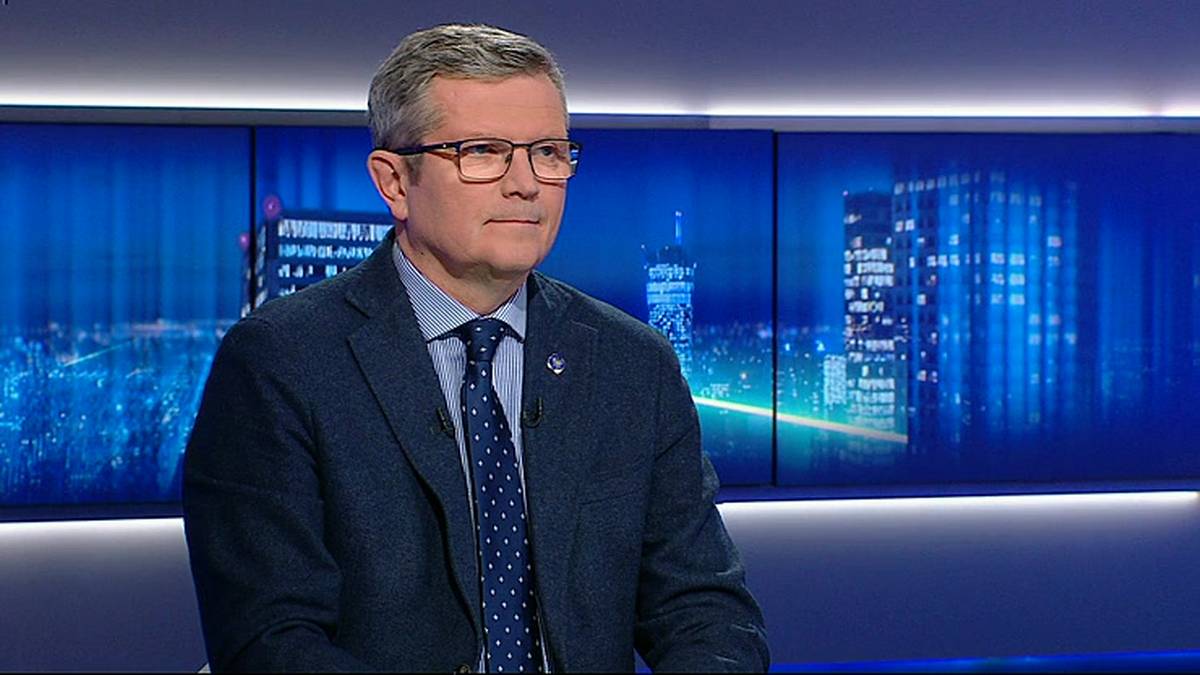 Mężczyzna w garniturze i krawacie, w okularach, siedzi, z poważną miną.